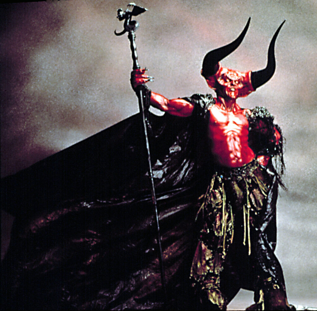 Tim Curry in full red, horned makeup and prosthetics as the Lord of Darkness in 